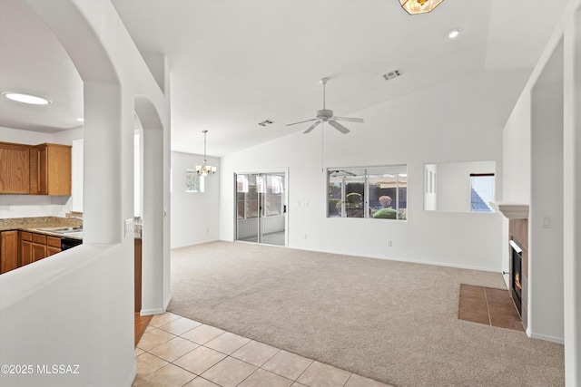 kitchen featuring vaulted ceiling, sink, light colored carpet, a fireplace, and ceiling fan with notable chandelier