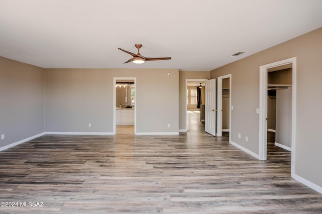 unfurnished bedroom featuring a spacious closet, hardwood / wood-style floors, ensuite bath, a closet, and ceiling fan