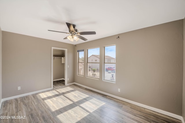 unfurnished bedroom featuring wood-type flooring, a closet, ceiling fan, and a walk in closet