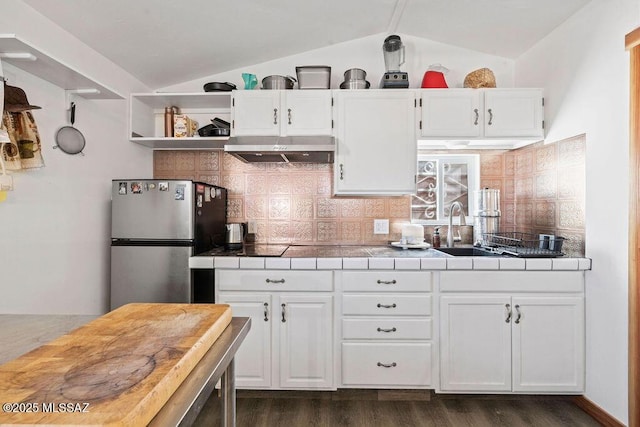 kitchen with tasteful backsplash, white cabinetry, vaulted ceiling, stainless steel fridge, and tile counters