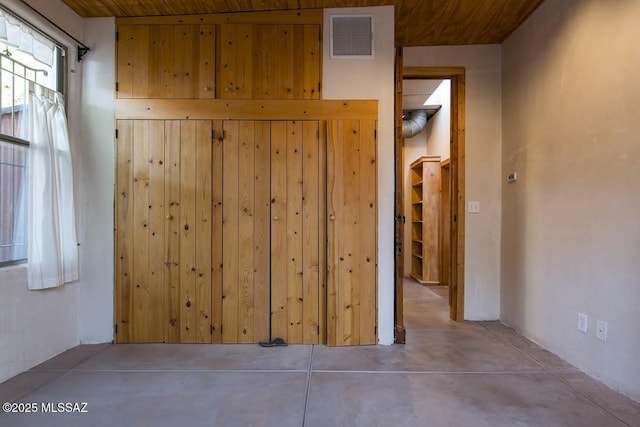 hallway featuring wooden ceiling, wooden walls, and concrete flooring