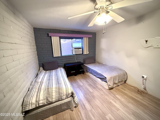 bedroom with cooling unit, ceiling fan, brick wall, and light hardwood / wood-style floors