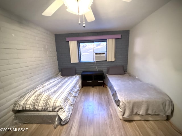 unfurnished bedroom with hardwood / wood-style flooring, brick wall, cooling unit, and ceiling fan