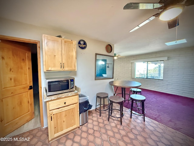 kitchen featuring ceiling fan, brick wall, and light brown cabinets