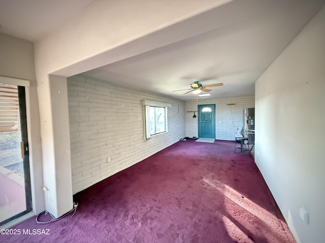 unfurnished living room featuring dark carpet, ceiling fan, and brick wall