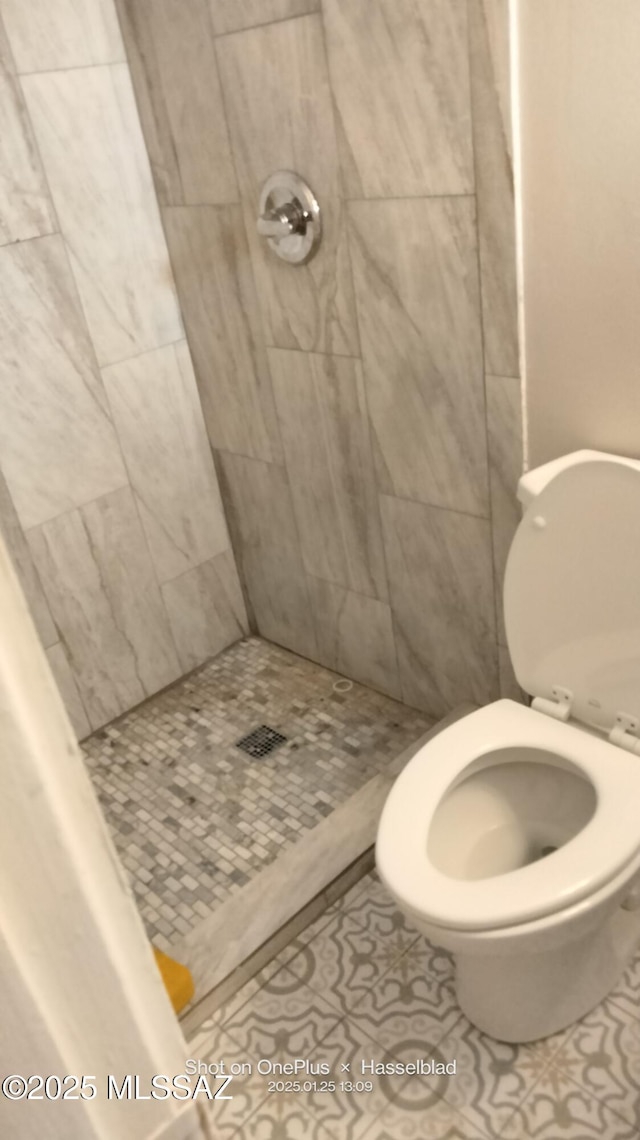 bathroom with tiled shower, toilet, and tile patterned flooring