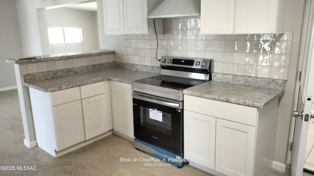 kitchen with electric stove, light tile patterned floors, white cabinets, kitchen peninsula, and wall chimney exhaust hood