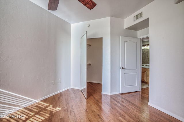 unfurnished bedroom featuring hardwood / wood-style flooring, a closet, ceiling fan, and a spacious closet