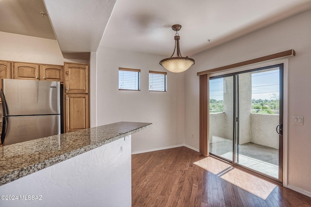 kitchen featuring pendant lighting, light stone counters, stainless steel fridge, and dark wood-type flooring