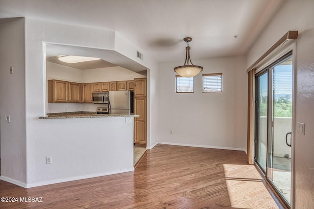 kitchen featuring hanging light fixtures, appliances with stainless steel finishes, kitchen peninsula, light stone countertops, and hardwood / wood-style floors