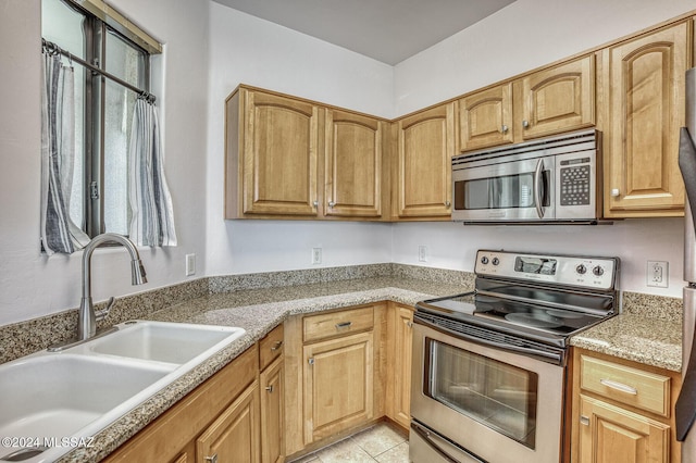 kitchen with appliances with stainless steel finishes, sink, light tile patterned floors, and light stone counters