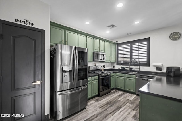kitchen featuring green cabinets, a sink, dark countertops, visible vents, and appliances with stainless steel finishes