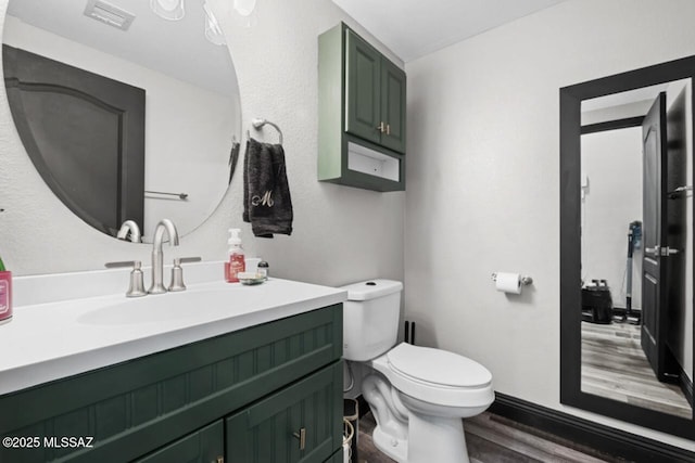half bathroom featuring visible vents, toilet, vanity, and wood finished floors