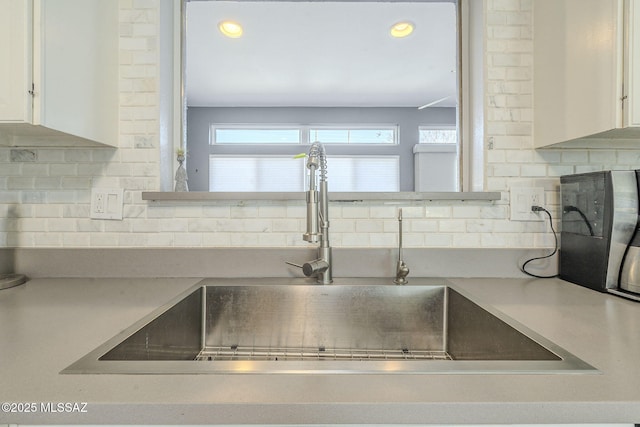 room details featuring sink, decorative backsplash, and white cabinets