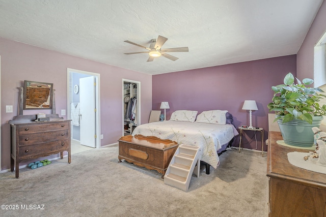 carpeted bedroom with connected bathroom, a walk in closet, a textured ceiling, a closet, and ceiling fan