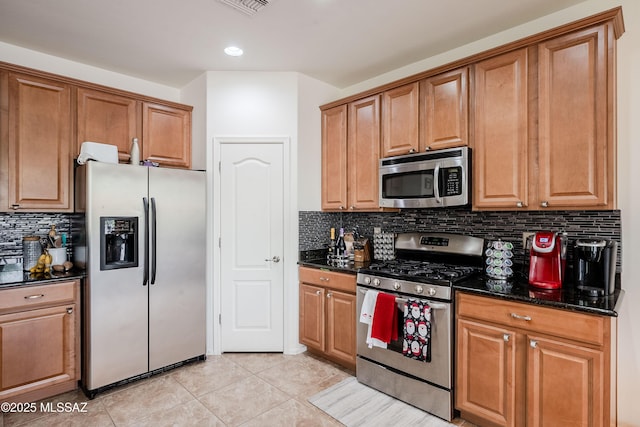 kitchen with stainless steel appliances, light tile patterned floors, decorative backsplash, and dark stone counters