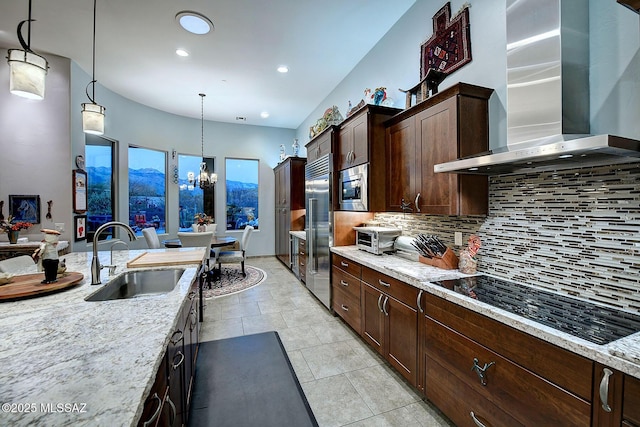 kitchen with light stone counters, wall chimney exhaust hood, built in appliances, and decorative light fixtures