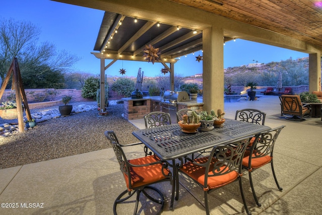 patio terrace at dusk featuring ceiling fan, a grill, exterior kitchen, and a mountain view