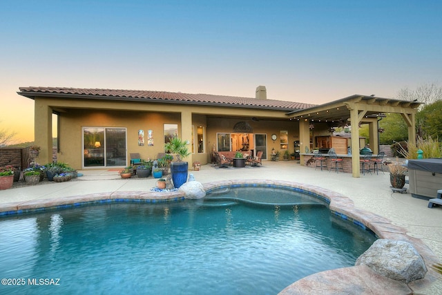 pool at dusk featuring a pergola, an outdoor kitchen, a patio, and exterior bar