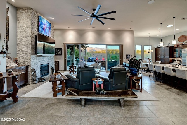 living room with a stone fireplace and ceiling fan with notable chandelier