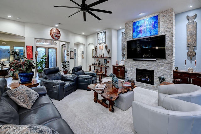 carpeted living room with a stone fireplace and ceiling fan