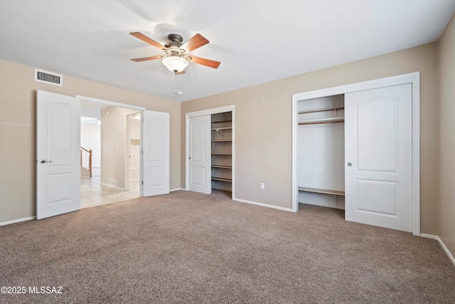 unfurnished bedroom featuring multiple closets, ceiling fan, and light colored carpet