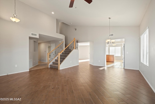 unfurnished living room featuring dark wood-type flooring, a towering ceiling, and ceiling fan with notable chandelier