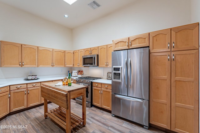 kitchen with a towering ceiling, stainless steel appliances, and hardwood / wood-style flooring