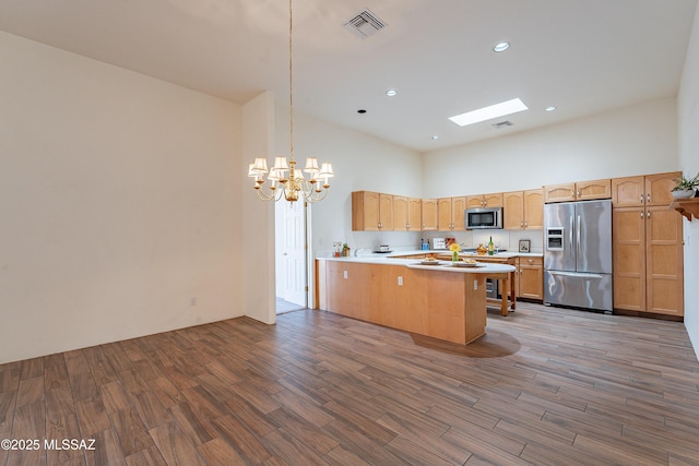 kitchen with appliances with stainless steel finishes, a towering ceiling, hardwood / wood-style floors, decorative light fixtures, and kitchen peninsula