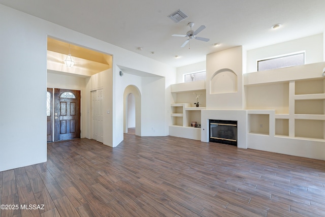 unfurnished living room with dark wood-type flooring, built in features, and ceiling fan