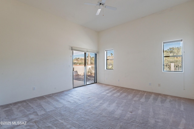 empty room with carpet floors, ceiling fan, and a towering ceiling