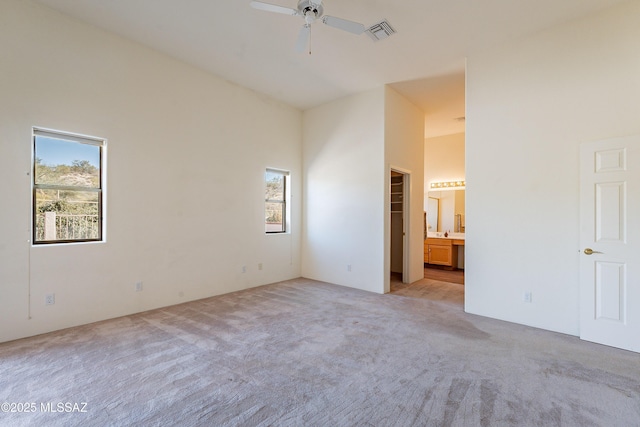 unfurnished bedroom with ensuite bath, light colored carpet, ceiling fan, and a towering ceiling