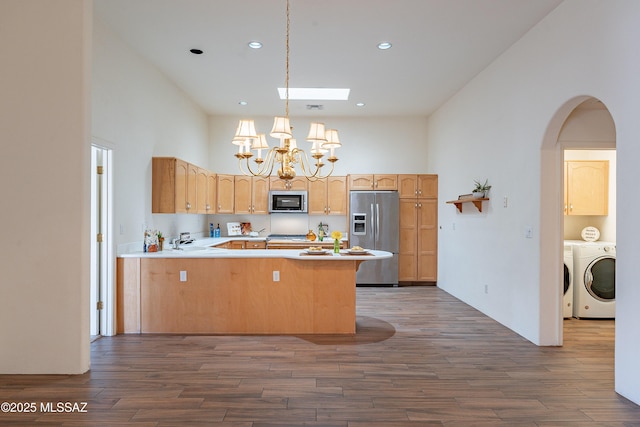 kitchen with dark wood-type flooring, washing machine and clothes dryer, hanging light fixtures, appliances with stainless steel finishes, and kitchen peninsula