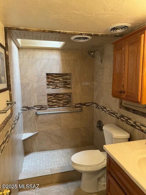 bathroom featuring a tile shower, vanity, tile patterned floors, and toilet