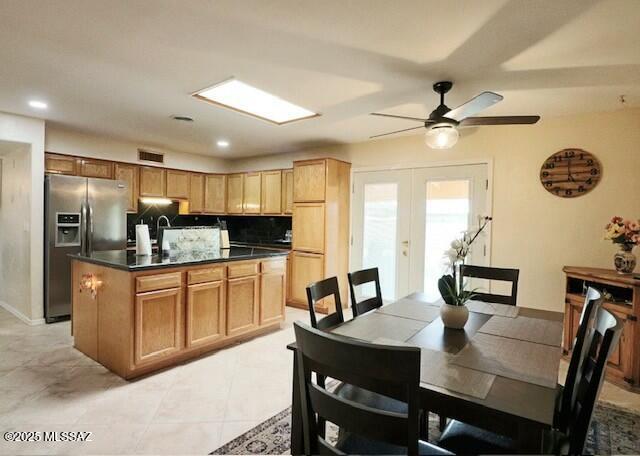 kitchen with ceiling fan, a kitchen island with sink, stainless steel fridge with ice dispenser, decorative backsplash, and french doors