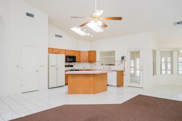 kitchen with a kitchen island, a skylight, decorative backsplash, light tile patterned floors, and white appliances