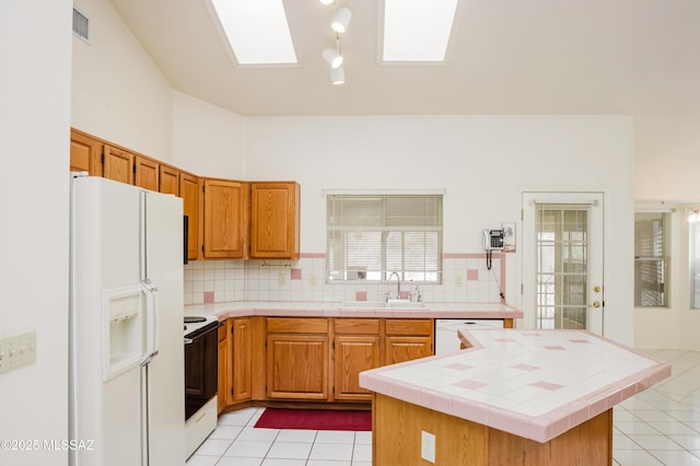 kitchen with sink, tile countertops, a skylight, white appliances, and decorative backsplash