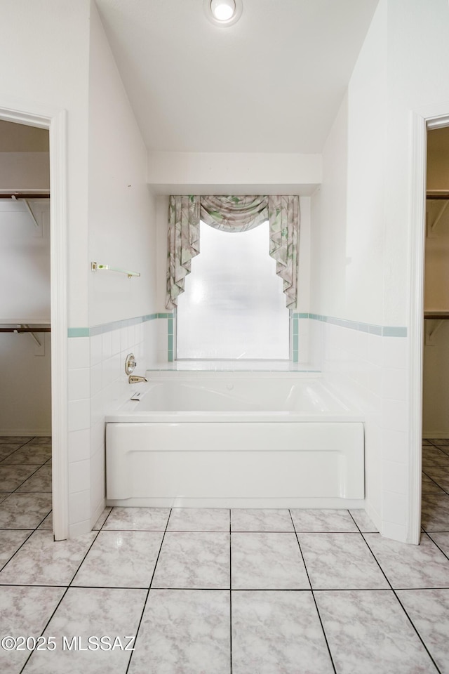 bathroom featuring tile walls, tile patterned flooring, vaulted ceiling, and a bathing tub