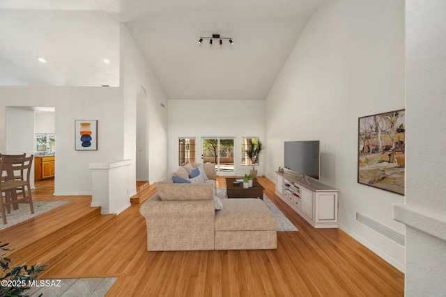 living room featuring plenty of natural light, light hardwood / wood-style floors, rail lighting, and a high ceiling