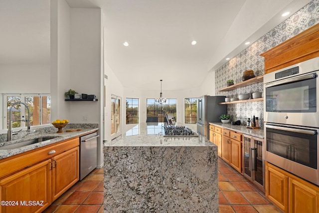 kitchen featuring light stone countertops, open shelves, a sink, appliances with stainless steel finishes, and a center island