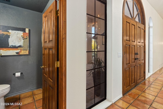 interior space with tile patterned floors, toilet, baseboards, and a textured wall