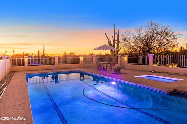 pool at dusk with a patio area, a fenced in pool, an in ground hot tub, and fence