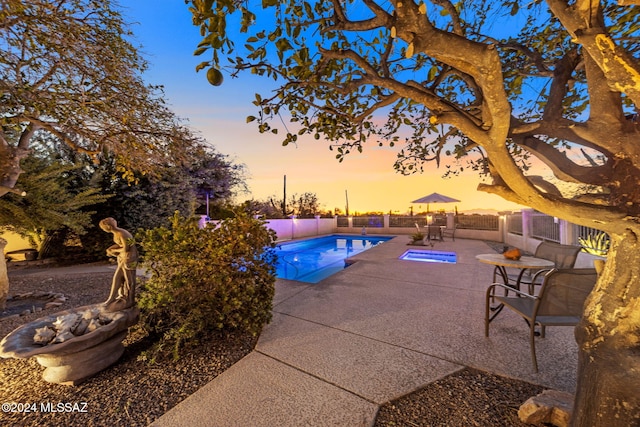 pool at dusk featuring a fenced in pool, fence, and a patio area