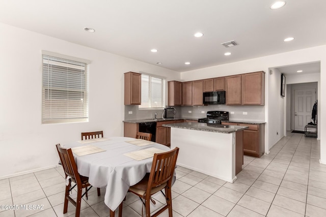 kitchen featuring a kitchen island, black appliances, light tile patterned flooring, decorative backsplash, and dark stone counters