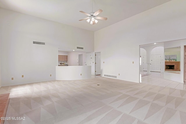 unfurnished living room featuring visible vents, light carpet, arched walkways, and ceiling fan