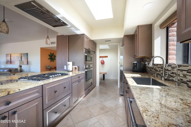 kitchen with sink, decorative light fixtures, light stone countertops, and appliances with stainless steel finishes