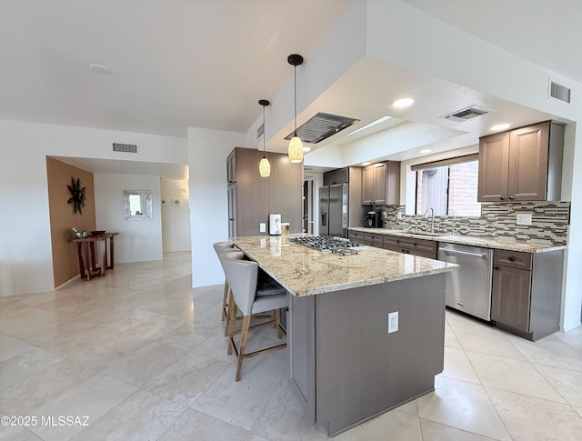 kitchen featuring a kitchen island, appliances with stainless steel finishes, decorative light fixtures, decorative backsplash, and light stone counters