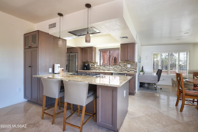 kitchen featuring appliances with stainless steel finishes, decorative light fixtures, tasteful backsplash, kitchen peninsula, and light stone countertops