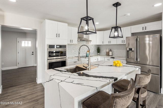 kitchen featuring stainless steel appliances, an island with sink, hanging light fixtures, and white cabinetry