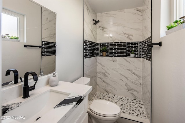 bathroom with tiled shower, vanity, and toilet